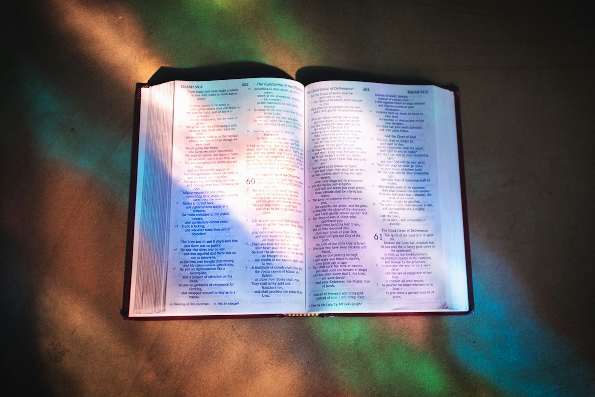 An open Bible lit by coloured light from a stained glass window