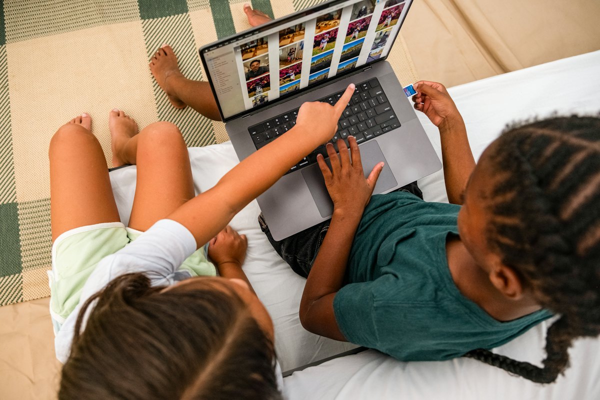 Two children sitting on a rug looking at a laptop together